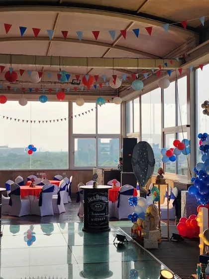 A wide view of the rooftop party space. The decor includes themed banners and lanterns, with seating arranged around a central glass-covered pool area, creating a unique and festive atmosphere.
