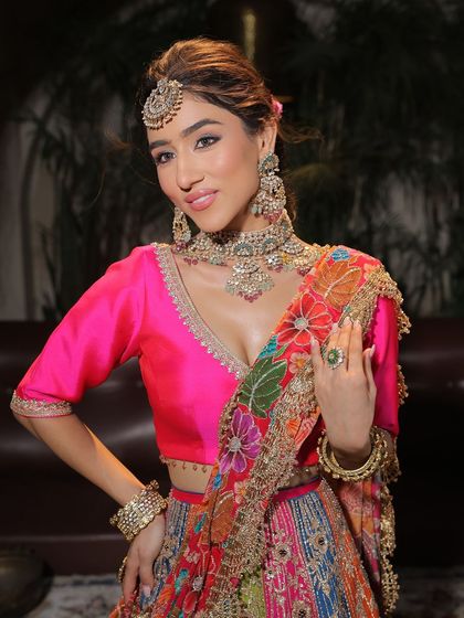 A portrait of a bride ready for her Mehendi. The makeup is fresh and vibrant, with a bright pink lip that beautifully contrasts with her multi-coloured lehenga.