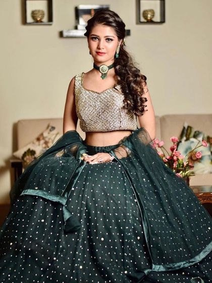 A seated portrait of the client in the dark green lehenga. The layered skirt creates a beautiful, full silhouette even while sitting.