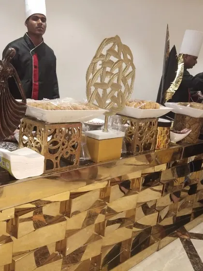 My chefs serving guests from a stylish golden buffet counter. The setup includes decorative sculptures and ornate serving dishes, adding an artistic touch to the food service area.