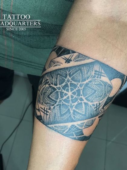A wide armband tattoo with a complex mandala and geometric design, showcasing intricate dotwork and shading.