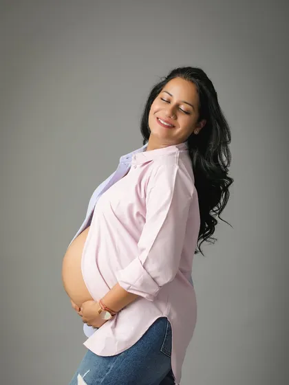 The pure joy and glow of motherhood. This mom-to-be looks so happy and relaxed in a casual open shirt and jeans, showing off her beautiful bump in a simple studio portrait.