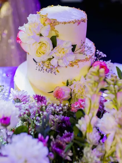 A beautiful two-tiered wedding cake, adorned with fresh flowers and gold leaf, ready for the couple's reception or Sangeet celebration.