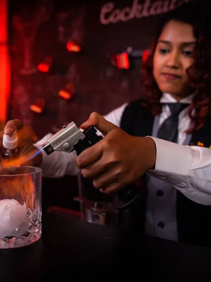We use innovative techniques to create unforgettable flavor profiles. Here, one of our mixologists uses a culinary torch to add a smoky aroma to a cocktail, demonstrating the artistry and attention to detail that goes into every drink we serve.