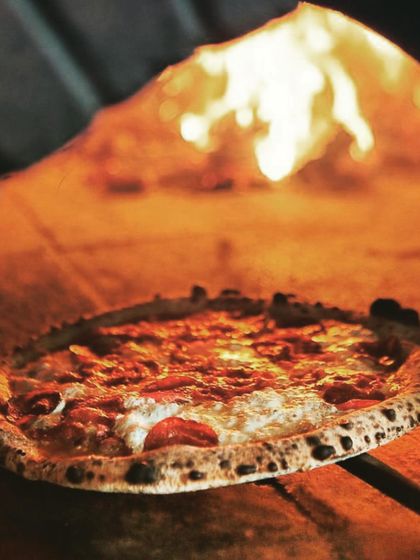 A classic pepperoni pizza baking next to the open flames. This shot captures the intense heat of the wood-fired oven, which is the secret to a quick bake and an incredible crust.