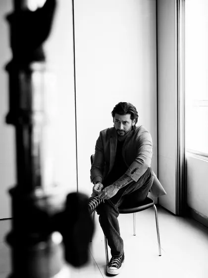 A candid, behind-the-scenes style black and white shot. The framing with the light stand adds a cool, industrial-chic element.