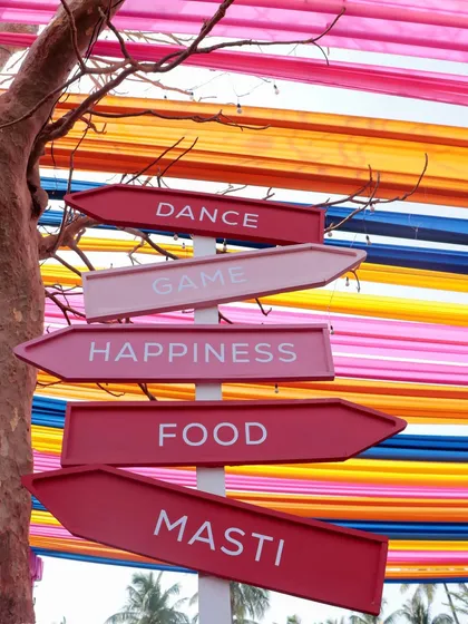 Playful directional signs pointing to 'Dance', 'Game', 'Happiness', 'Food', and 'Masti', guiding guests through the fun-filled activities at the Haldi event.