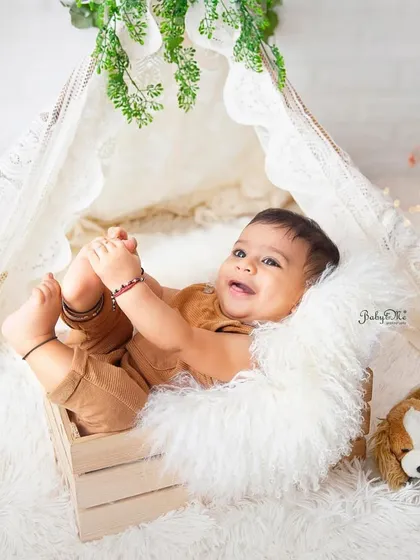 Grabbing his toes and smiling, this is a classic happy baby pose. The warm tones of his outfit match the cozy boho theme perfectly.