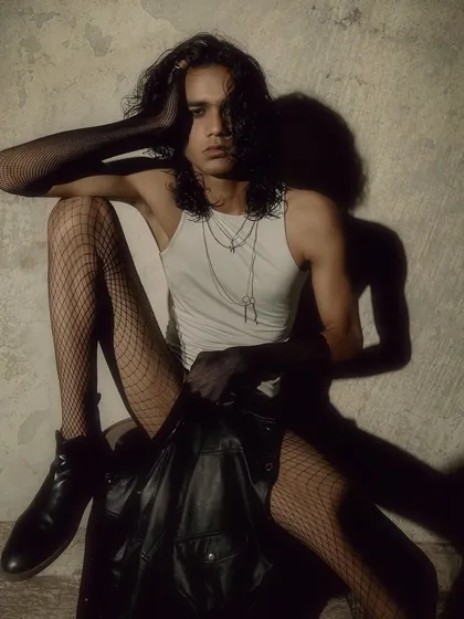 A full-body shot from a gothic-inspired editorial. The styling, with fishnets and a leather jacket, is combined with a moody, textured background to create a dark and alternative fashion story.