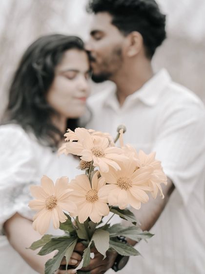 A creative shot focusing on a bouquet of yellow flowers, with the couple sharing a romantic kiss in the blurred background.