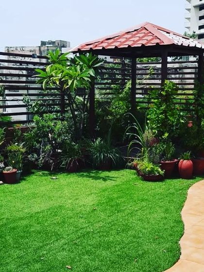 A beautiful and lush terrace garden filled with a variety of plants in terracotta pots, a wooden gazebo, and a winding pathway.