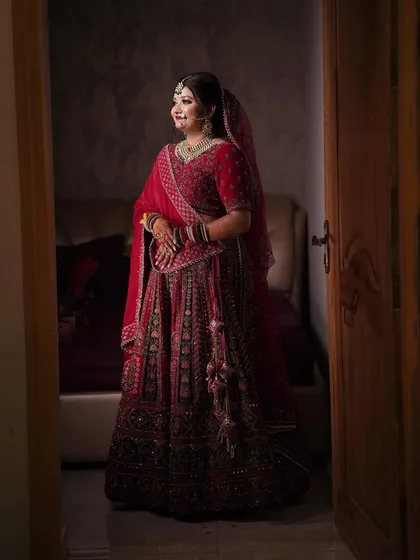 A classic bridal portrait taken through a doorway, capturing the bride in her beautiful red lehenga.