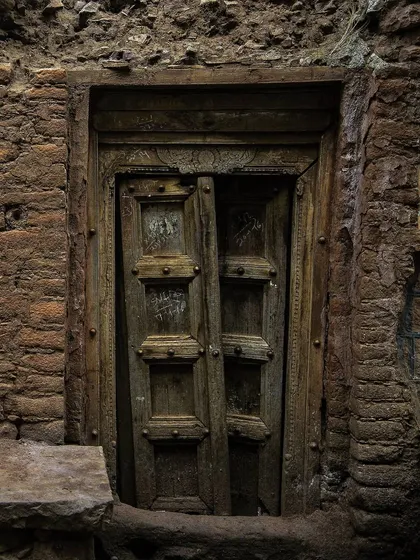 Tucked into a mud-brick wall, this dark, intricately carved wooden door is slightly ajar. The deep shadows and earthy tones give it a timeless and almost secretive quality.