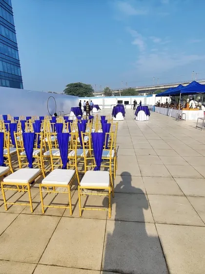 For corporate clients like Indigo Airlines, we execute professional outdoor events with precision. This rooftop setup features neatly arranged Chiavari chairs with custom blue fabric, reflecting the company's branding against a clean, urban backdrop.