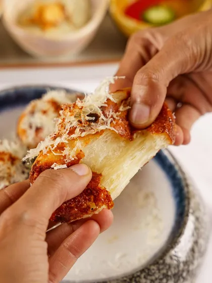 Tearing into a piece of cheesy garlic bread. This close up action shot is all about the soft, fluffy texture of the bread and the melted cheese, creating a powerful sensory appeal.