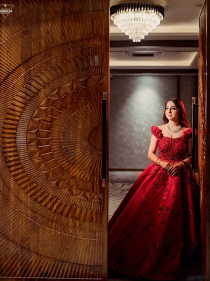 A stunning portrait of the bride in a vibrant red gown, her regal pose framed by an ornate wooden door.