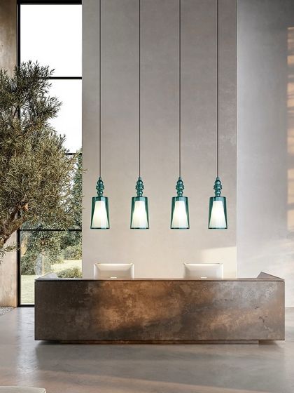 A row of four Alibaglass pendants in a striking turquoise green hangs over a reception desk, demonstrating how color can be used to make a bold design statement in a commercial space.
