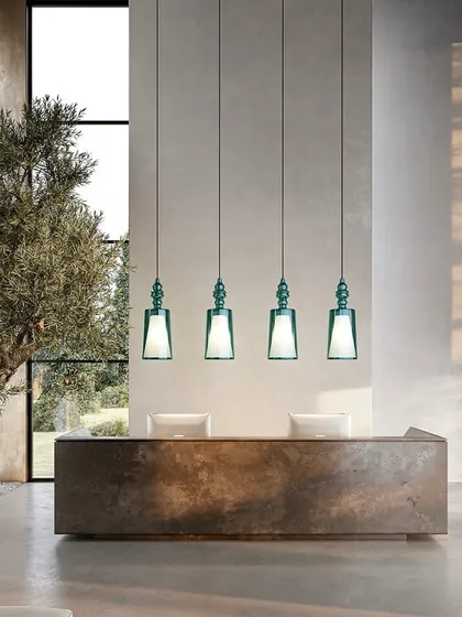 A row of four pendants in a striking green glass, installed over a reception desk. This demonstrates their suitability for commercial and hospitality applications, adding a touch of color and sophistication.