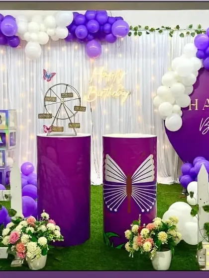 A royal purple butterfly theme with a white curtain backdrop. The decoration includes a Ferris wheel prop and large, colorful butterfly cutouts.