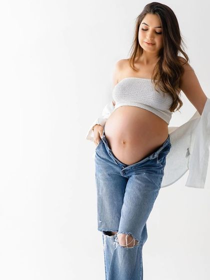 A quiet, contemplative solo portrait. This image beautifully captures the mother's connection with her baby bump in a simple, unposed moment.