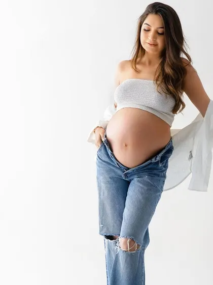 A quiet, contemplative solo portrait. This image beautifully captures the mother's connection with her baby bump in a simple, unposed moment.