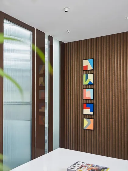 Texture adds depth and character. In this director's cabin, a fluted wooden accent wall is paired with vibrant, colorful abstract art, creating a focal point that is both professional and inspiring.