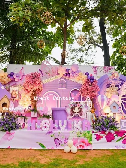 A daytime view of Nishvika's fairy garden party, showcasing the vibrant purple and pink color scheme, the detailed fairy house, and the custom name display.