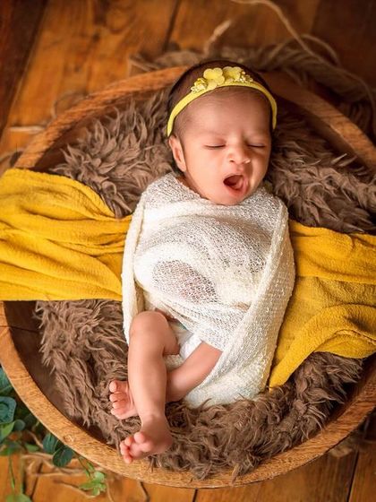 A sleepy yawn from a baby tucked into a wooden bowl with yellow and white fabrics. These candid moments during a posed session are always precious.