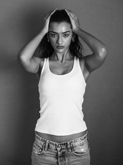 A strong, confrontational pose captured in high-contrast black and white. The lighting creates dramatic shadows that emphasize the model's physique and intense expression. This is a powerful, modern portrait.