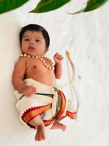 A sweet baby dressed as Little Rama, lying down with a small bow and arrow.
