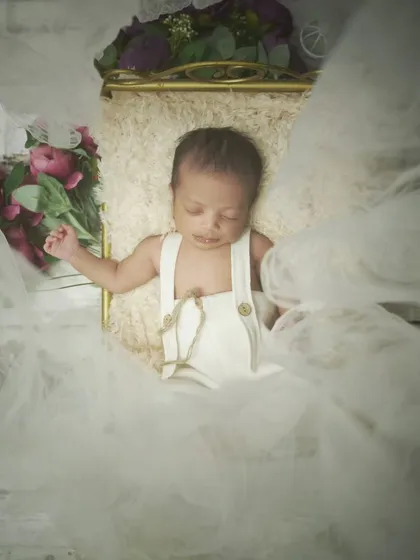 Another angle of the newborn in white overalls, surrounded by soft, white tulle. This creates an angelic and ethereal feel.