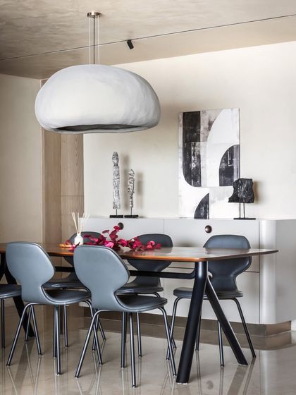 A bespoke, monolithic pendant light hangs over the dining table, its rustic finish echoing the raw beauty of the nearby staircase. This piece enhances the sculptural quality of the space and reinforces the home's curated, artistic feel.