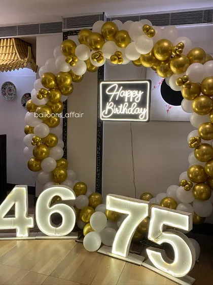 For milestone birthdays, I create stunning photo backdrops like this one. It features a full circular balloon arch in elegant gold and white, a custom 'Happy Birthday' neon sign, and large illuminated marquee numbers.