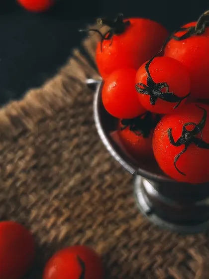 A close-up of vibrant cherry tomatoes in a metal cup on a burlap surface, highlighting their freshness with a rustic touch.