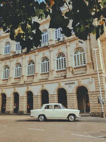 A classic white Ambassador car, the original king of Indian roads, parked in front of the Hermes store. A beautiful study in contrasts.