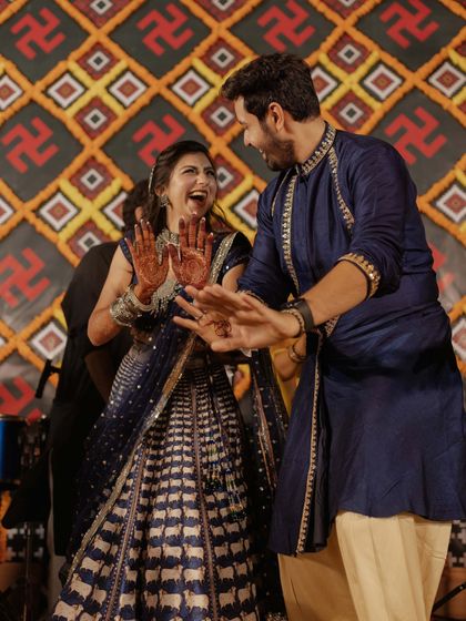 The couple sharing a laugh on the dance floor, their coordinated blue outfits looking stunning against the backdrop of the patola-inspired decor.