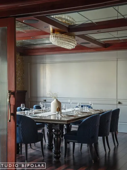 In contrast, the family dining area is designed for a cozier, more intimate feel. Deep blue chairs, rich wood tones, and a mirrored ceiling with a crystal chandelier create a warm and moody atmosphere.