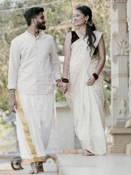 A beautiful shot of a couple in matching white and gold traditional outfits, walking hand-in-hand at a temple-themed location, perfect for a cultural pre-wedding session.