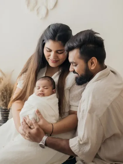 A beautiful family portrait capturing the new parents admiring their sleeping baby, swaddled and safe in their arms.