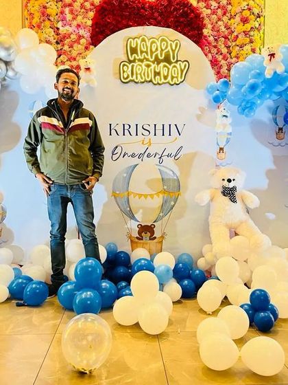 Our decorator stands proudly in front of a "Krishiv is Onederful" birthday setup. This hot air balloon theme features a beautiful backdrop with blue and white balloon clouds and teddy bear props.