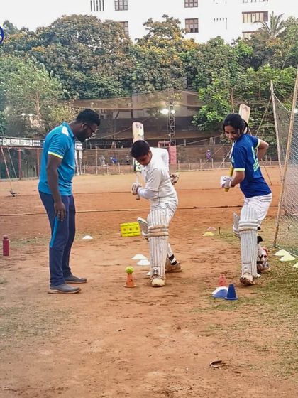 A coach provides feedback to two young players during a net session. This close interaction is crucial for personalized skill development and building player confidence.