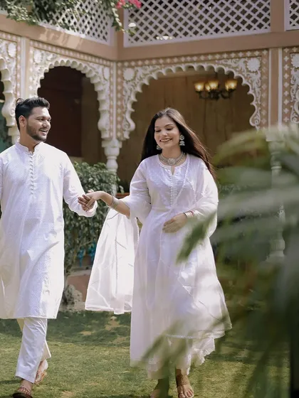 A happy, candid moment of the couple walking through the gardens of a heritage-style venue. Their coordinated white outfits create a look of pure elegance for this pre-wedding shoot.