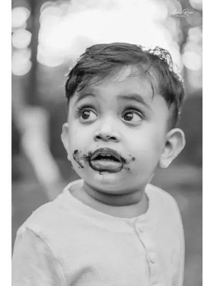 This black and white close-up of Ivaan after his cake smash is full of character. The monochrome treatment emphasizes his wide, curious eyes and the delightful chocolatey mess.