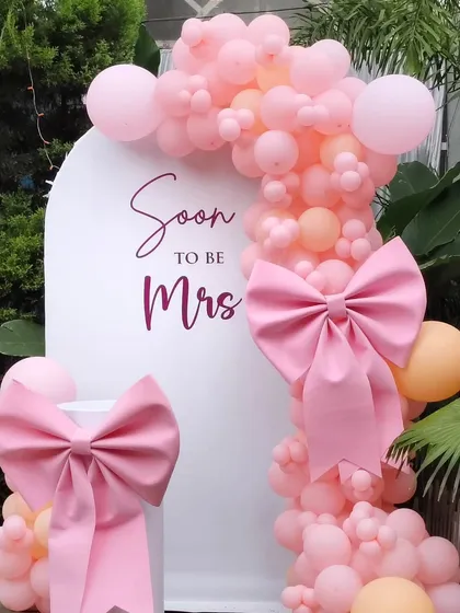 This 'Soon to be Mrs' bridal shower setup is a favorite for its feminine charm. I used a clean white arch backdrop, a lush garland of pink and peach balloons, and finished it with oversized pink bows for a touch of playful elegance.