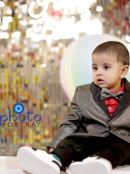 A handsome little boy in his formal suit and bow tie, sitting in front of a sparkling backdrop at his first birthday party.