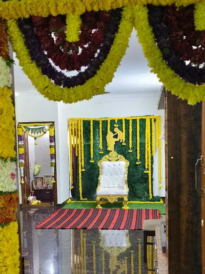 A complete baby shower setup viewed from the entrance of the room. The decoration includes a throne chair placed against a green backdrop with hanging yellow flower strings.