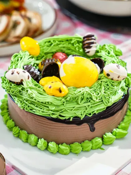 A playful Easter-themed cake decorated with green frosting to look like grass and topped with chocolate eggs. The close-up shot highlights the fun and festive details of the design.