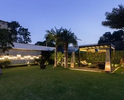 An evening view of a residential lawn, where architectural lighting plays a key role. The wall features a dynamic pattern of light, while uplighting on trees and the pergola creates depth and drama, showcasing our expertise in garden lighting design.