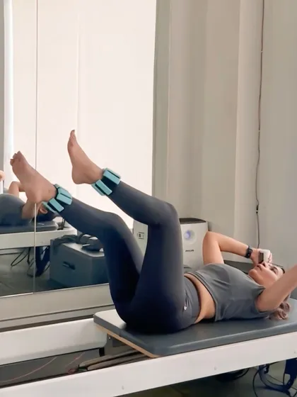 A client performs leg lifts with ankle weights on the reformer carriage. This exercise is excellent for targeting the lower abdominals and hip flexors with precision.