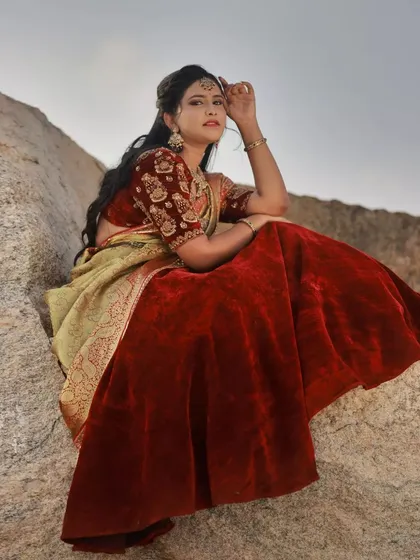 A seated portrait on a large boulder. The soft, natural light of the evening sky complements the rich red velvet of the lehenga and the intricate ethnic jewellery.